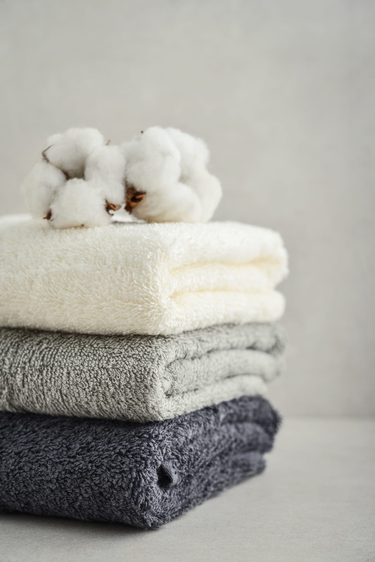 Stack,Of,Bath,Towels,With,Cotton,Flowers,On,Light,Concrete