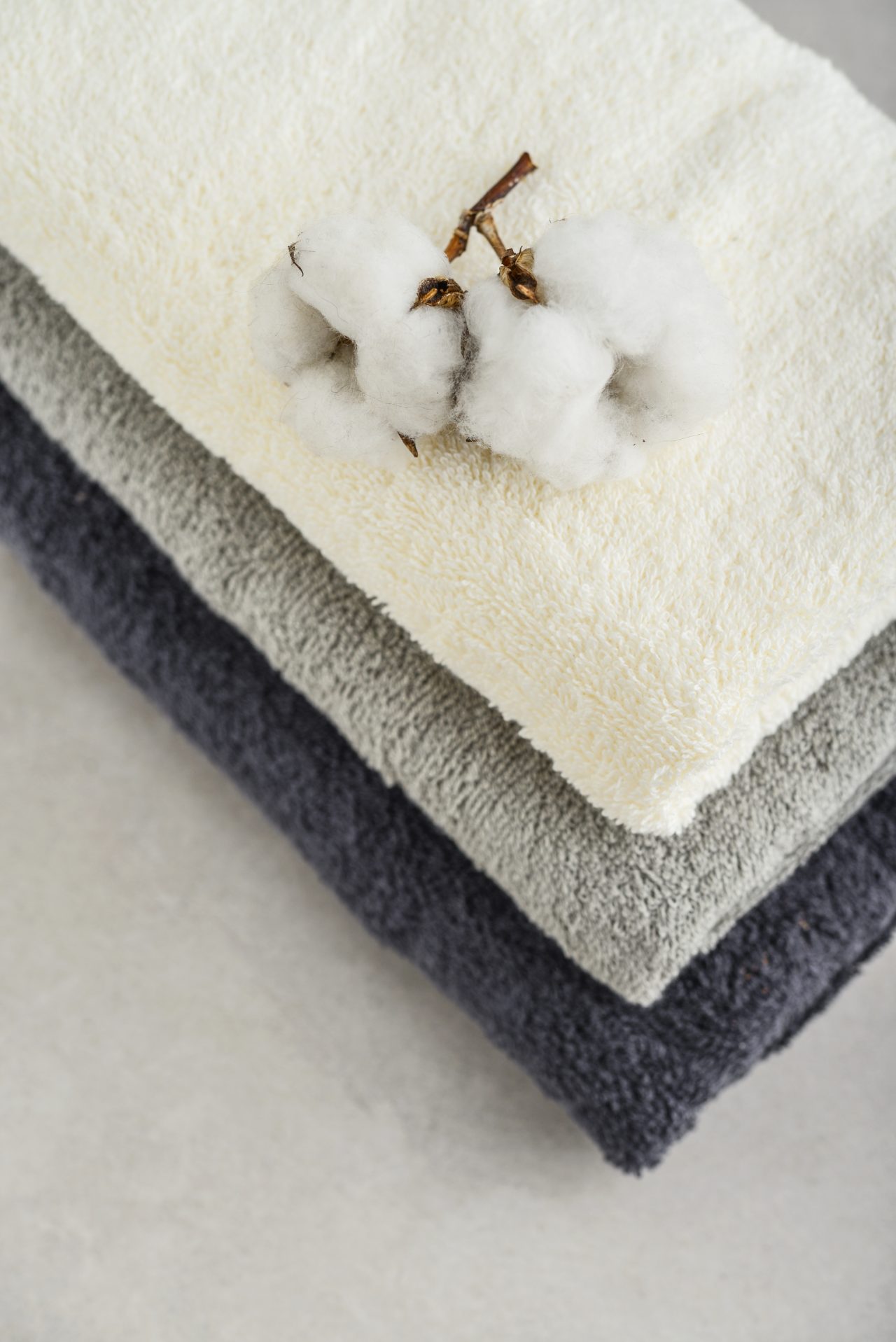 Stack,Of,Bath,Towels,With,Cotton,Flowers,On,Light,Concrete